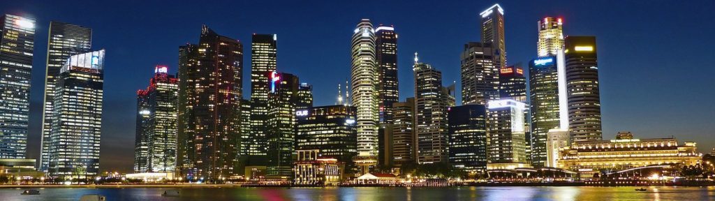 A city skyline at night, with lights reflecting on water in the foreground 